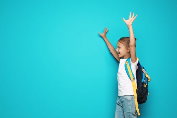 Little school child with backpack on color background